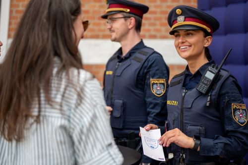 Eine Polizistin überreichen einer Passantin den Folder 'Coffee with cops'