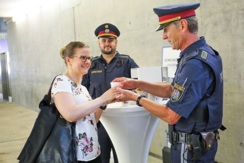 Zwei Polizisten überreichen einer Passantin einen Kaffee