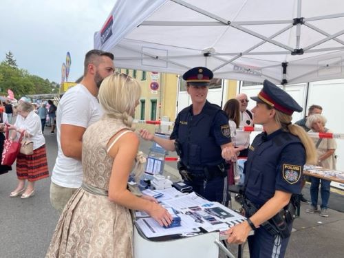 Polizistinnen und Polizisten vor dem Informationsstand am Neustifter Kirtag mit Besuchern, Foto: BK